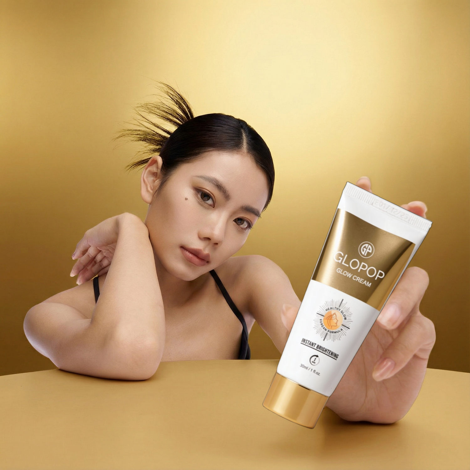 Woman holding a tube of Glopop Glow Cream against a gold background